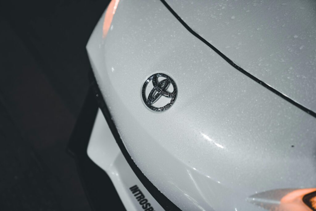 Detailed shot of a wet white car bonnet featuring the Toyota logo, highlighting texture and shine.